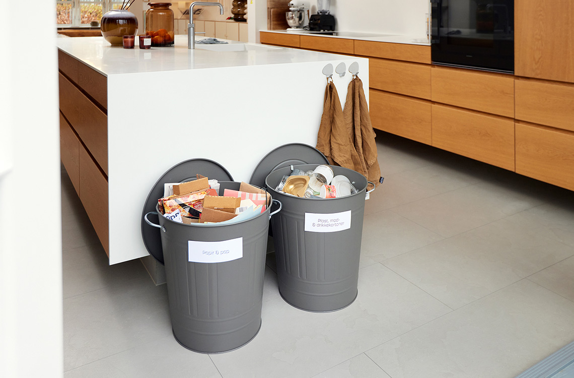 To grå spande til affaldssortering står på gulv forenden af køkkenbord